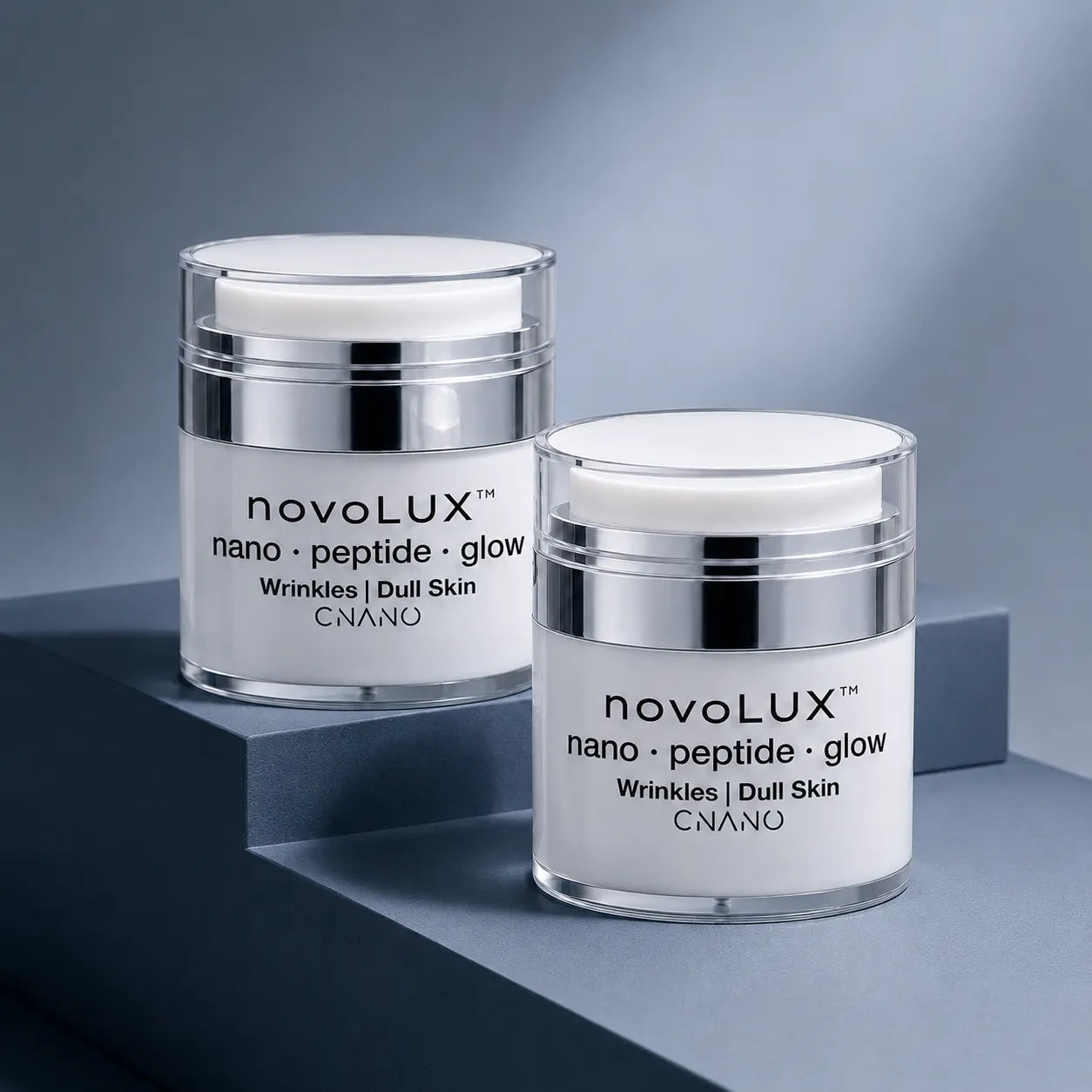 Two white and silver cosmetic jars of CNANO novoLUX nano peptide glow cream arranged on a modern gray geometric platform.