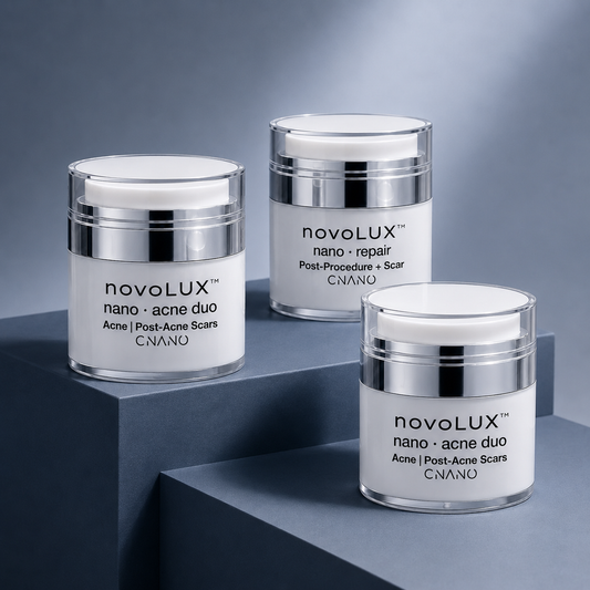 Three white and silver jars of CNANO nanoLUX skincare products arranged on dark gray geometric blocks against a blue-gray background.