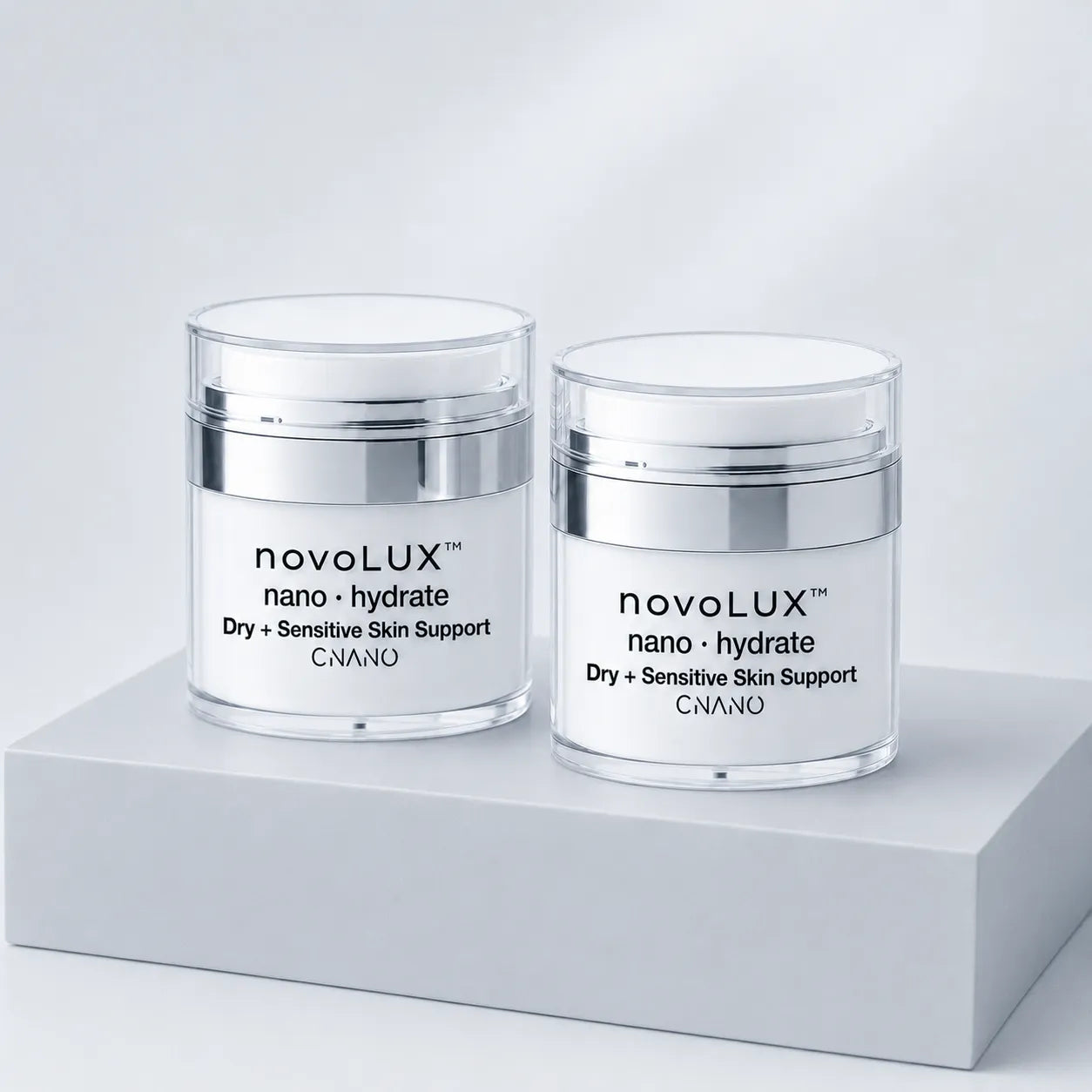 Two clear cosmetic jars with white lids and silver bands, labeled novoLUX nano hydrate, displayed on a light gray pedestal against a soft white background.
